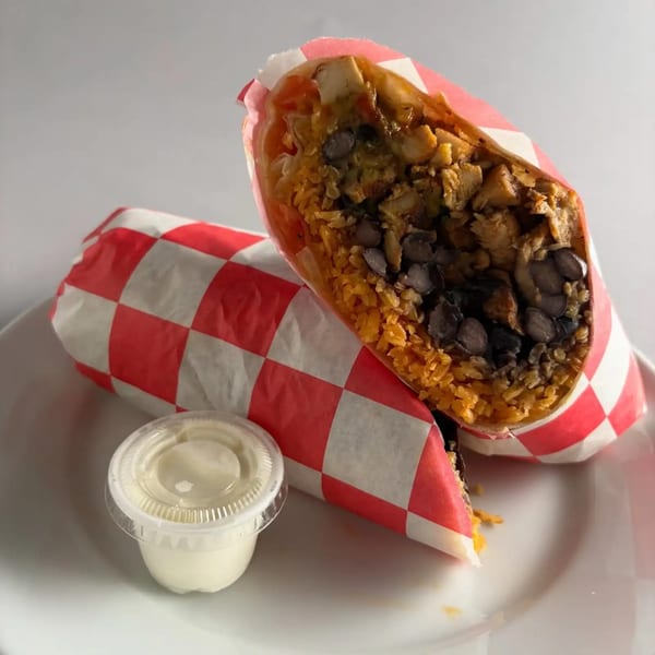 Two Folklore Artisanal Mexican burritos, one cut open to show chicken, rice, and black beans, with a side of sauce.
