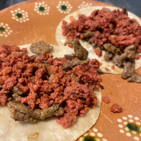 Two Folklore Artisanal Mexican tacos with red chorizo and steak on a decorative orange plate.