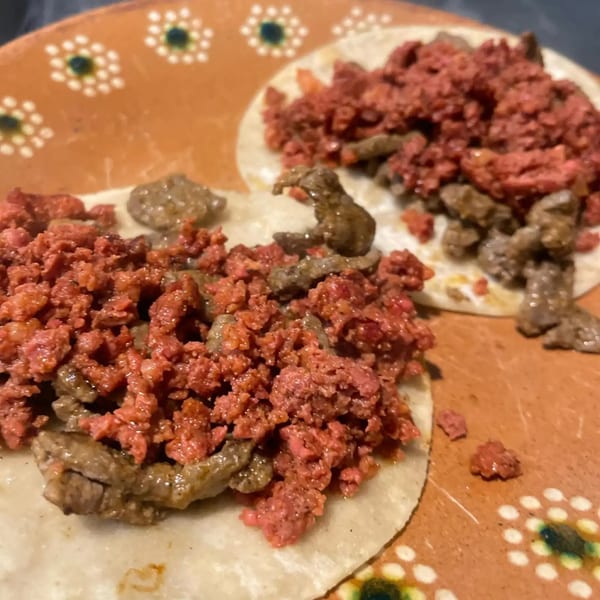 Two Folklore Artisanal Mexican tacos with red and brown meat on a decorative orange plate.