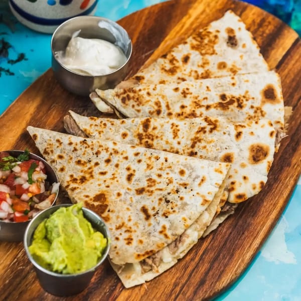 Quesadillas with sides of guacamole, salsa, and sour cream on a wooden board.