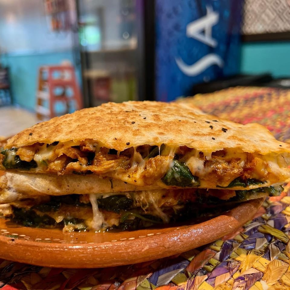 A cheesy, golden-brown quesadilla filled with chicken and spinach, served on a rustic plate.