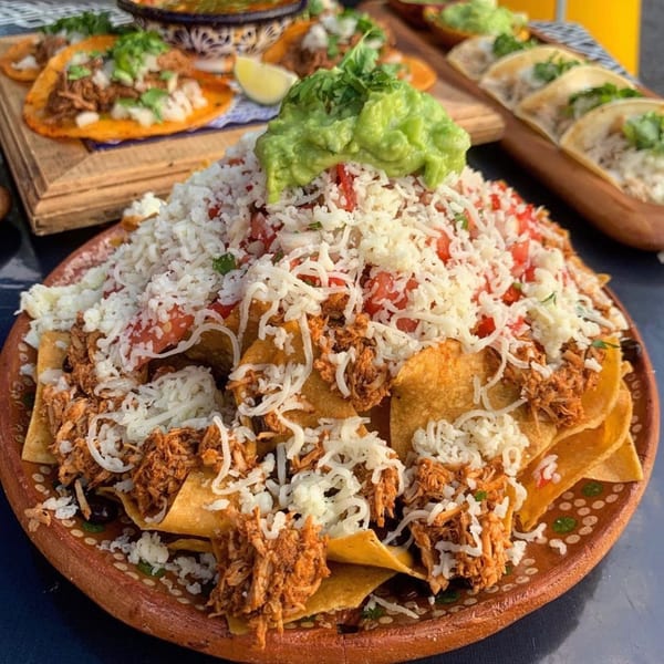 A large plate of Folklore Artisanal Mexican nachos with shredded chicken, cheese, tomatoes, and guacamole.