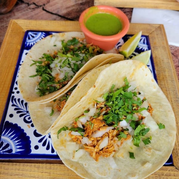 Three Folklore Artisanal Mexican tacos with chicken, onions, and cilantro, served with green salsa and lime.