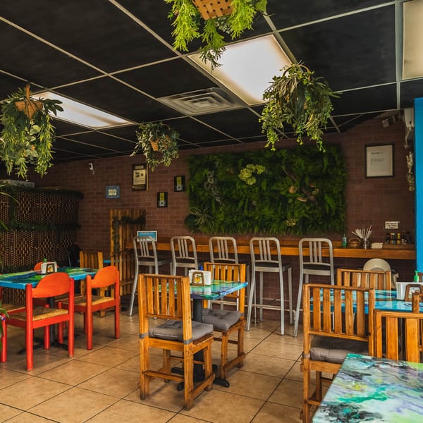Folklore Artisanal Mexican restaurant interior with colorful tables, wooden chairs, and a green plant wall.