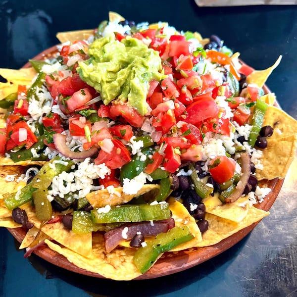 A large plate of Folklore Artisanal Mexican nachos with guacamole, pico de gallo, and black beans.