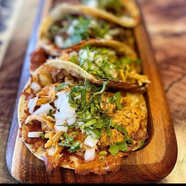 Four chicken tacos with cilantro and onions on a wooden serving board at Folklore Artisanal Mexican.