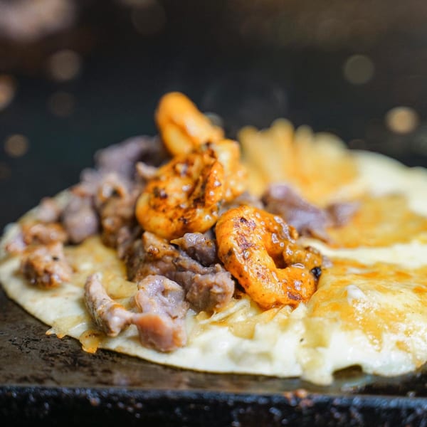 A close-up of a sizzling Mexican quesadilla with steak, shrimp, and melted cheese.