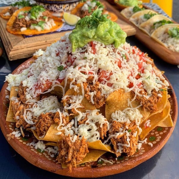 A large plate of Folklore Artisanal Mexican nachos with shredded chicken, cheese, and guacamole.